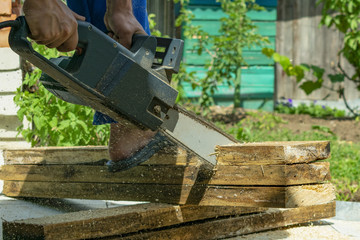 man in blue work clothes cuts pine boards with electric hand saw, close-up