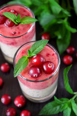 Two layered smoothie in glasses surrounded by cranberries and mint against the dark background
