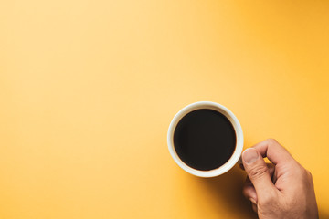 Hand of a man holding a hot black coffee cup on yellow background