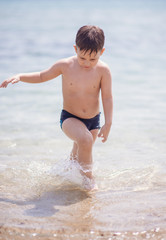 Adorable boy standing in the water on the beach. Family vacation or holiday concept.