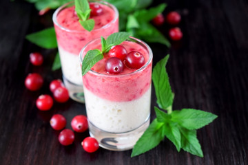 Two layered smoothie in glasses surrounded by cranberries and mint against the dark background