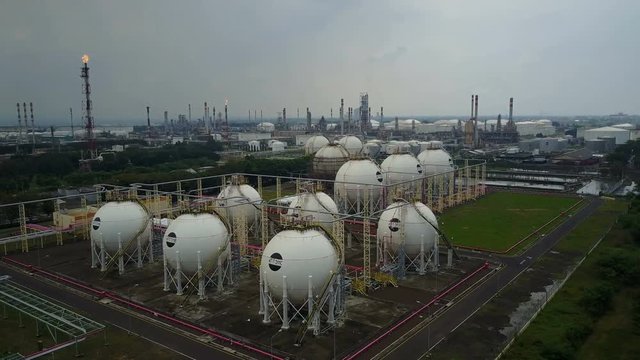 Flying over spherical gas storage tanks towards huge petrochemical facility and oil refinery in central Java, heavy industry Indonesia