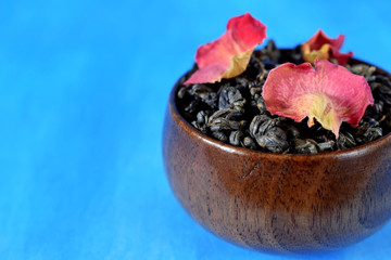 Leaf green tea with dried rose petals in a wooden bowl against the blue background. Copy space