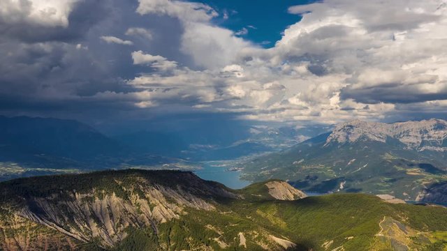 Elevated timelapse view of Serre-Poncon Lake, Savines-le-Lac and the Grand Morgon peak with passing clouds in Summer. Hautes-Alpes, Durance Valley, Southern French Alps, France