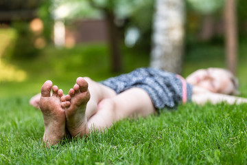 Girl lying on the grass, dirty feet on foreground - obrazy, fototapety, plakaty
