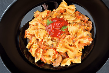 Delicious Farfalle Pasta in a bolognese sauce with ketchup and herbs on a black plate. Top view