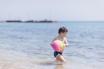Adorable boy having fun on the beach with a ball on a summer day. Family vacation or holiday concept.