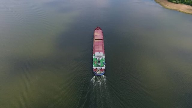 An amazing bird`s eye view of a cargo barge moving slowly in the middle of the Dnipro river and leaving a white waterway in summer