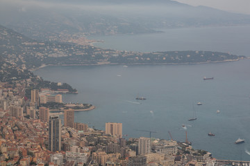 Scenic panorama of Monaco from the observation deck. Roofs of houses and buildings and hills on background. Sailing boats and yacht harbour, port. Aerial top view, foggy morning. France