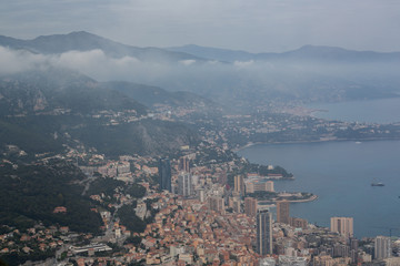 Scenic panorama of Monaco from the observation deck. Roofs of houses and buildings and hills on background. Sailing boats and yacht harbour, port. Aerial top view, foggy morning. France