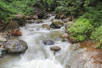 Little waterfall in mountain forest with silky foaming water and wet stones