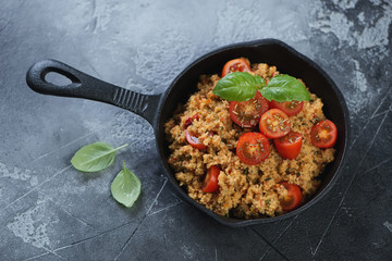 Cast-iron pan with cuscus and tomatoes on a grey weathered concrete background, high angle view