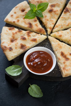 Sliced ossetian pie with fresh green basil and sauce, closeup, selective focus