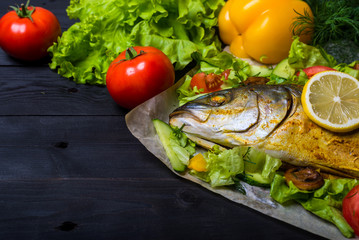 Baked sea fish with vegetables on a wooden table, free space.