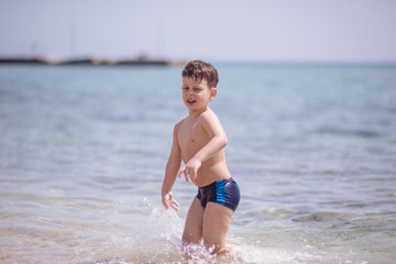 Adorable boy standing in the water on the beach. Family vacation or holiday concept.