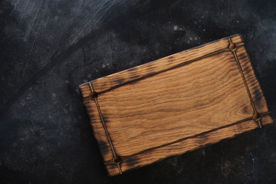 Rustic wooden serving tray on a dark scratched metal background, horizontal shot, top view, copyspace