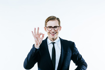 Portrait of a young man in suit and tie making a 'perfect' hand gesture, on white studio background