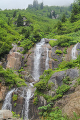 Fototapeta na wymiar Waterfall in mountain forest with silky foaming water and wet stones