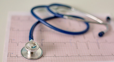 closeup of the desk of a doctors office with a stethoscope in the foreground and a bottle with pills in the background, selective focus