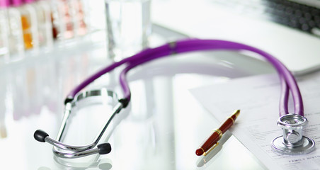 closeup of the desk of a doctors office with a stethoscope in the foreground and a bottle with pills in the background, selective focus