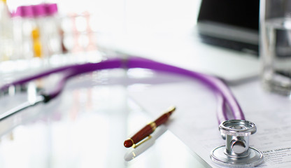 closeup of the desk of a doctors office with a stethoscope in the foreground and a bottle with pills in the background, selective focus