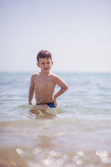 Fototapeta na wymiar Adorable boy standing in the water on the beach. Family vacation or holiday concept.