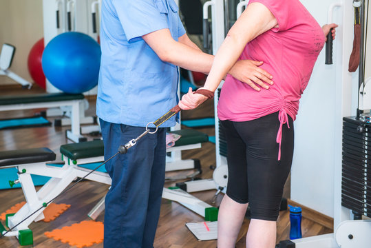 No Face Elderly Woman Doing Active, Special Exercises Guided By Physical Therapist At The Hospital Rehabilitation Center. Osteopathy, Chiropractic, Physiotherapy. Selective Focus, Space For Text.