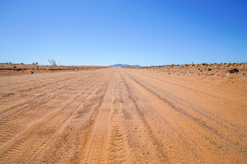Tyre tracks in dusty sand road stretching far ahead
