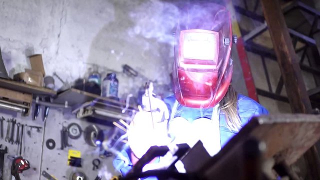 cute welder girl in uniform in the garage working with welding equipment. Women's work in art