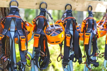 Gordijnen Climbing gear equipment - orange helmet harness zip line safety equipment hanging on a board. Tourist summer time adventure park family and company team building concept for extreme recreation sports © echobg