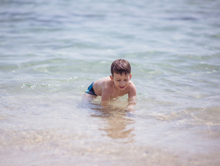 Adorable young kid sitting in the water on the beach