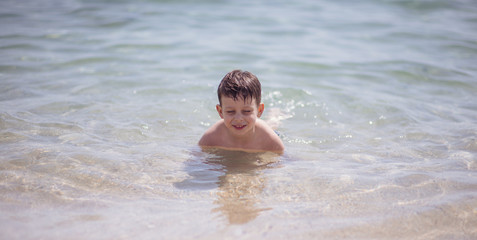 Adorable young kid sitting in the water on the beach