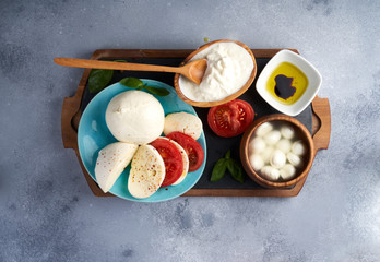 Italian soft cheeses plate. Mozzarella Buffalo, balls, Stracciatella, basil leaves, tomatoes, olive oil with vinegar on gray background. Top view, copy space.