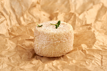 Fototapeta na wymiar Crottin cheese with thyme leaves on brown package paper.