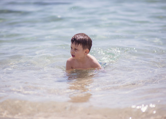 Adorable young kid sitting in the water on the beach