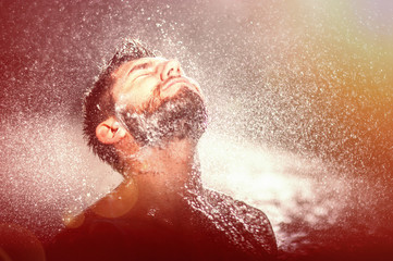 Handsome sexy bearded young man in shower, with water splashes into his face, dramatic red light (vintage effect)