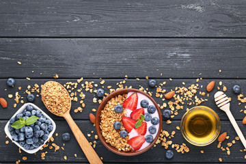 Tasty granola with berries in bowl and honey on black wooden table
