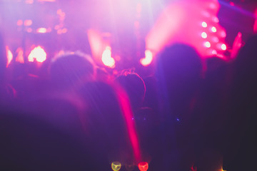 Fototapeta premium A crowded concert hall with scene stage lights, rock show performance, with people silhouette and hand holding smartphone