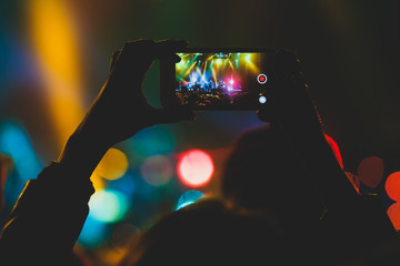 Fototapeta na wymiar A crowded concert hall with scene stage lights, rock show performance, with people silhouette and hand holding smartphone