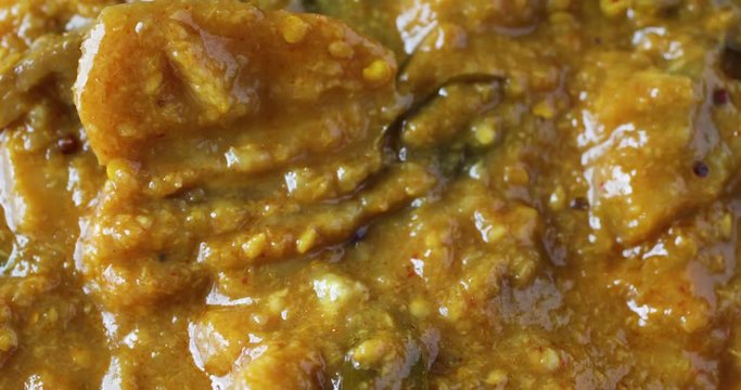 Closeup video of stirring then taking a fork full of eggplant curry with a white plastic fork.