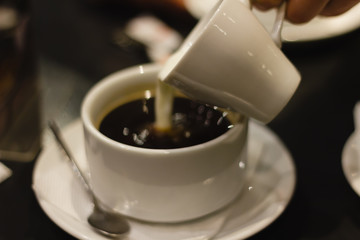 Milk is poured into a cup of coffee. Soft focus.