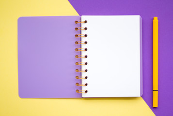 Top view flat lay picture with notepad as mockup for your design and different accessories on yellow and violet background.