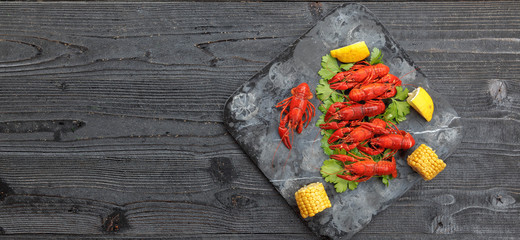 Red boiled crayfish with lemon, corn and parsley on stone slate tray on dark old rustic background © jarvna