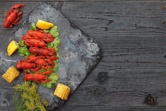 Red boiled crayfish with lemon, corn and parsley on stone slate tray on dark old rustic background