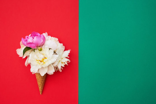 Waffle ice cream cones with white peony flowers on red green background. Summer concept. Copy space, top view