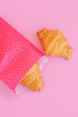 Fresh croissant in pink wrap on pink background