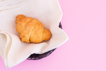 Fresh croissant in basket on pink background