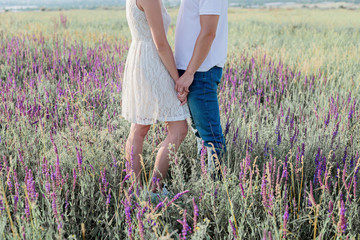 Cute young couple in love is holding their hands in a field of flowers