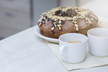 Homemade cake with nuts and chocolate and two cups with coffee on wooden white table