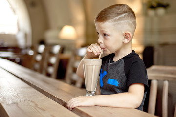 little boy drinking milkshake sitting at the table in cafe.